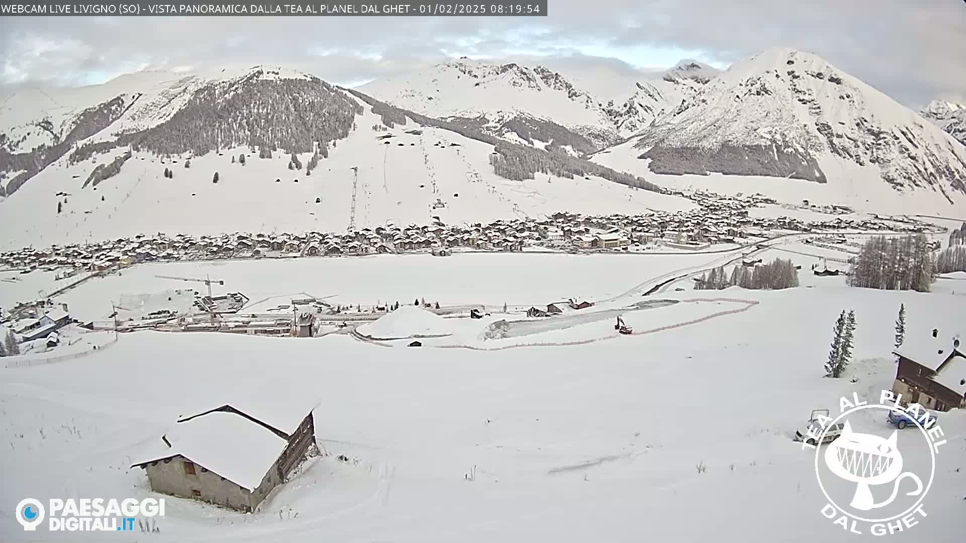 A snow-covered village nestled in a valley between snow-capped mountains under an overcast sky.