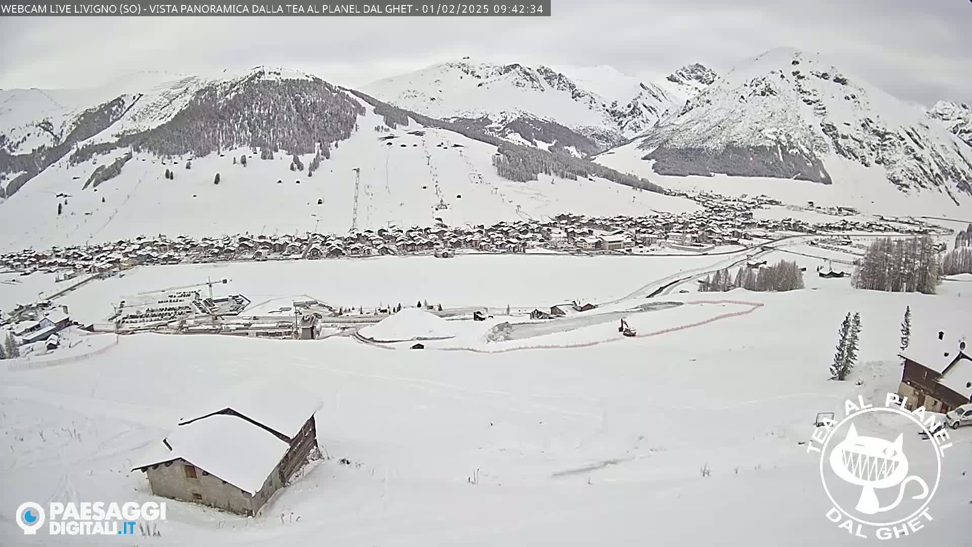 A snow-covered village nestled in a valley between snow-capped mountains under an overcast sky.