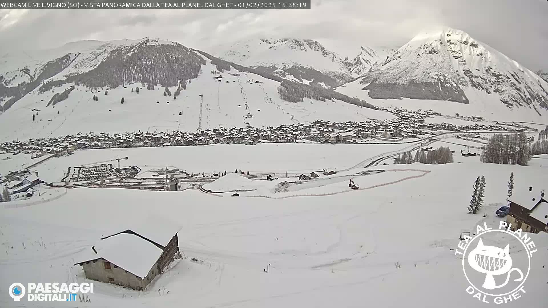 A snow-covered village nestled in a valley between snow-capped mountains under an overcast sky.