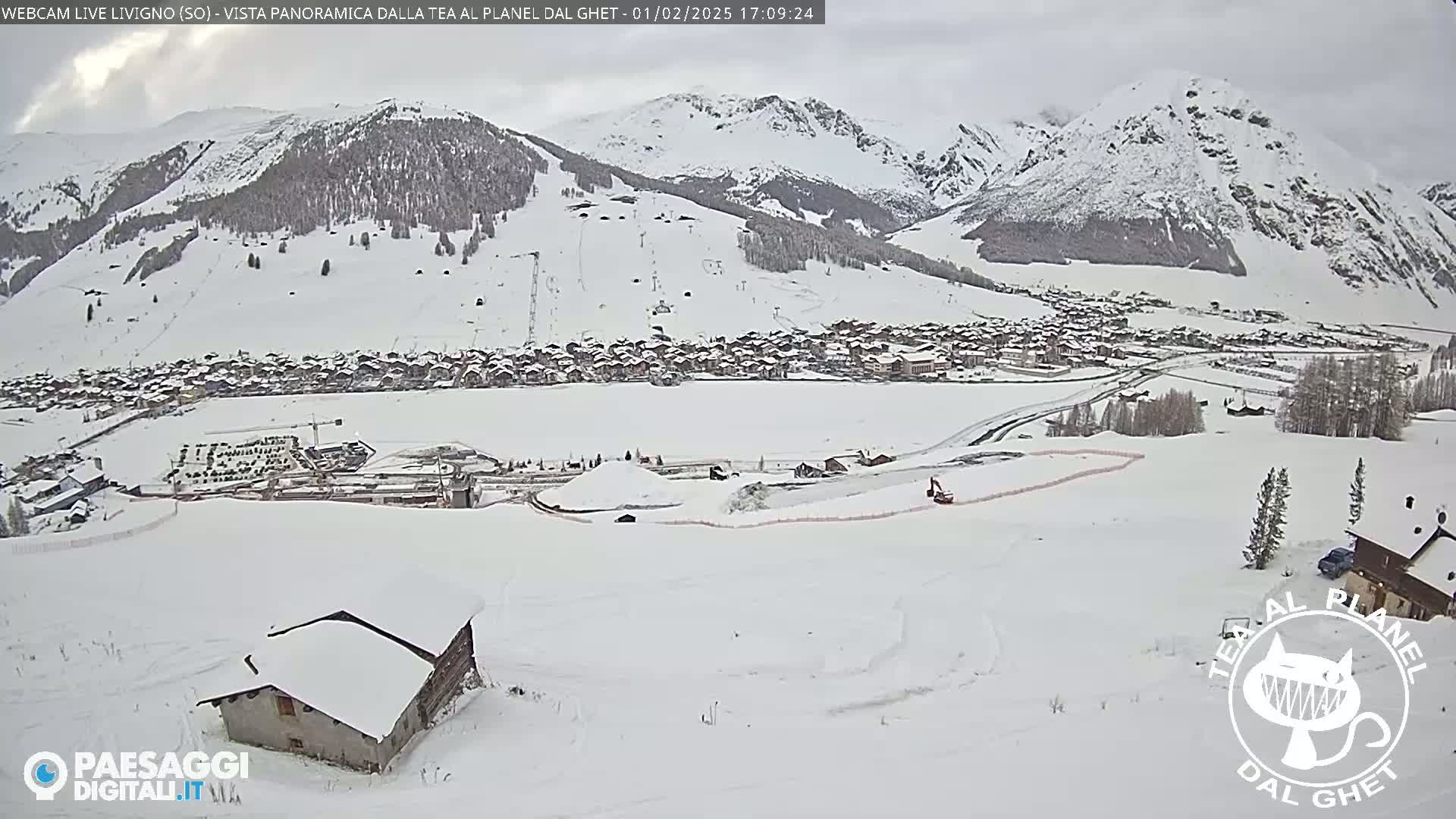 A snow-covered village nestled in a valley between snow-capped mountains under an overcast sky.