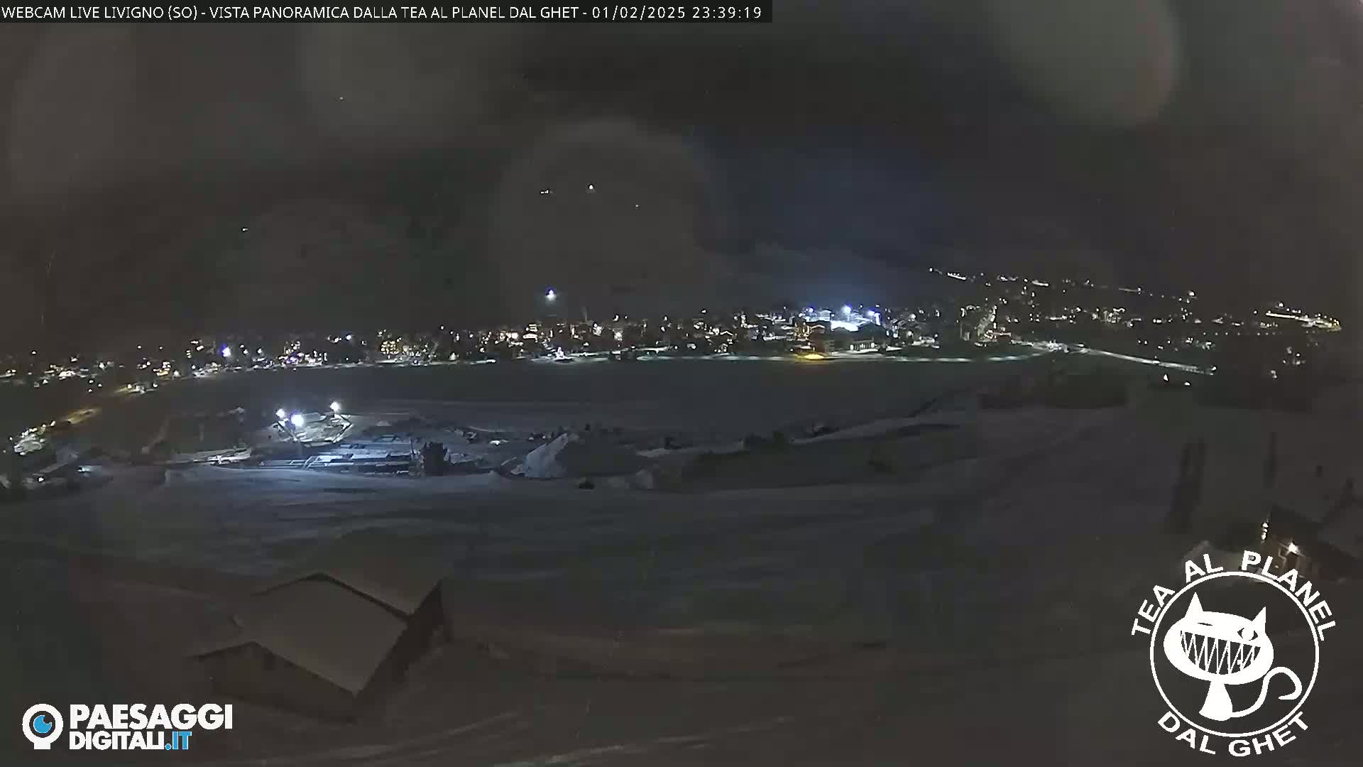 A nighttime, snow-covered landscape reveals a distant town illuminated with lights under a dark sky.