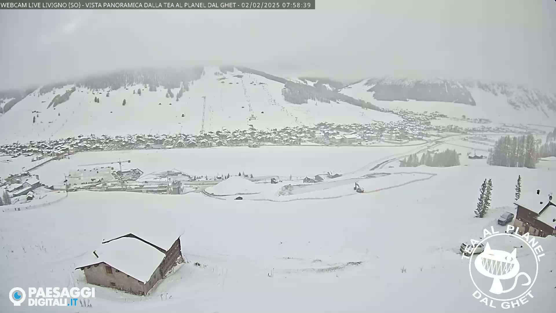 A snow-covered village nestled in a valley, with snow-covered hills and mountains in the background, during a snowstorm.