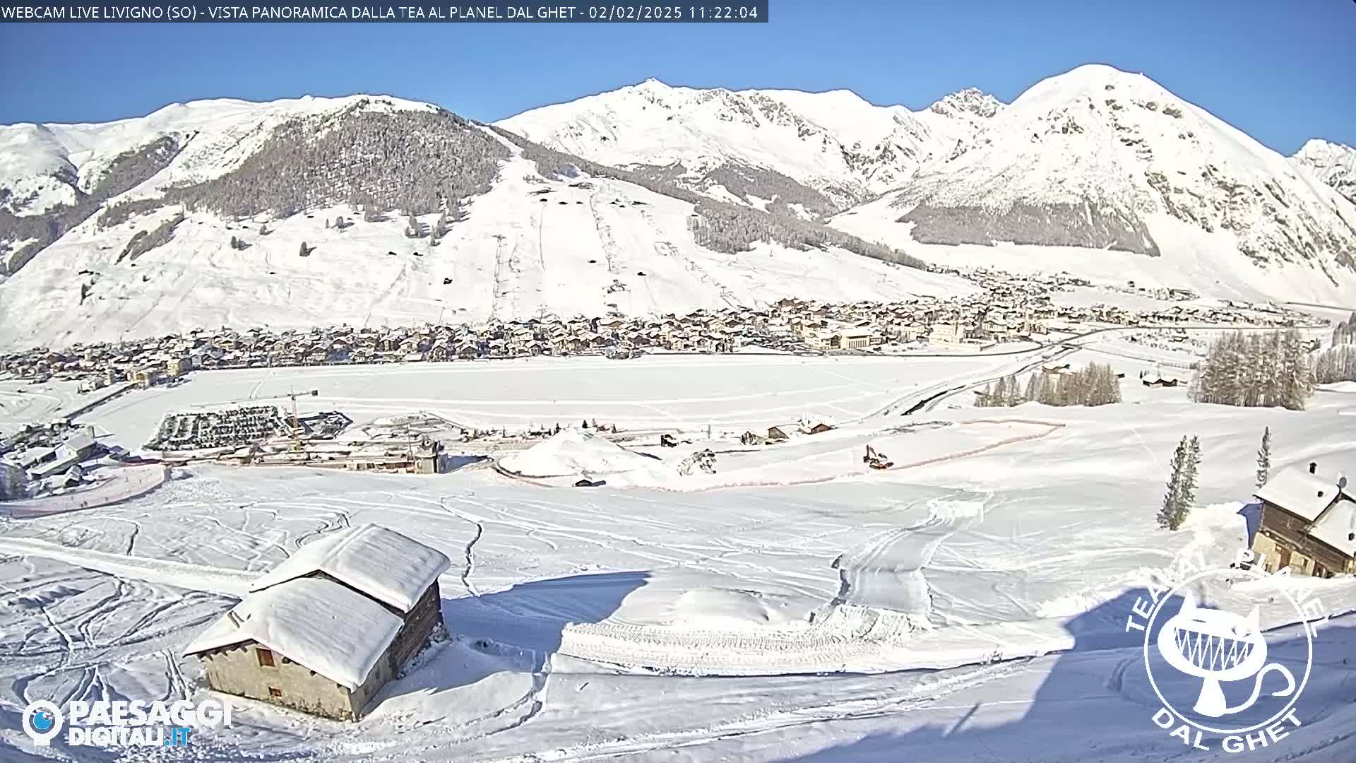 A snow-covered village nestled in a valley surrounded by snow-capped mountains under a bright, sunny sky.