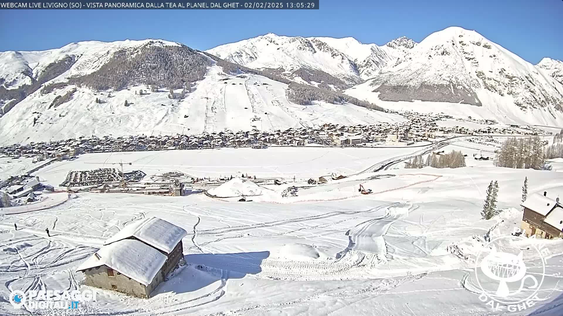 A snow-covered mountain village is nestled in a valley surrounded by snow-capped mountains under a bright, sunny sky.