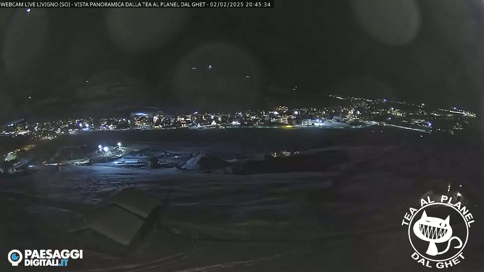 A nighttime, panoramic view of a snow-covered landscape shows a town illuminated with lights in the distance.