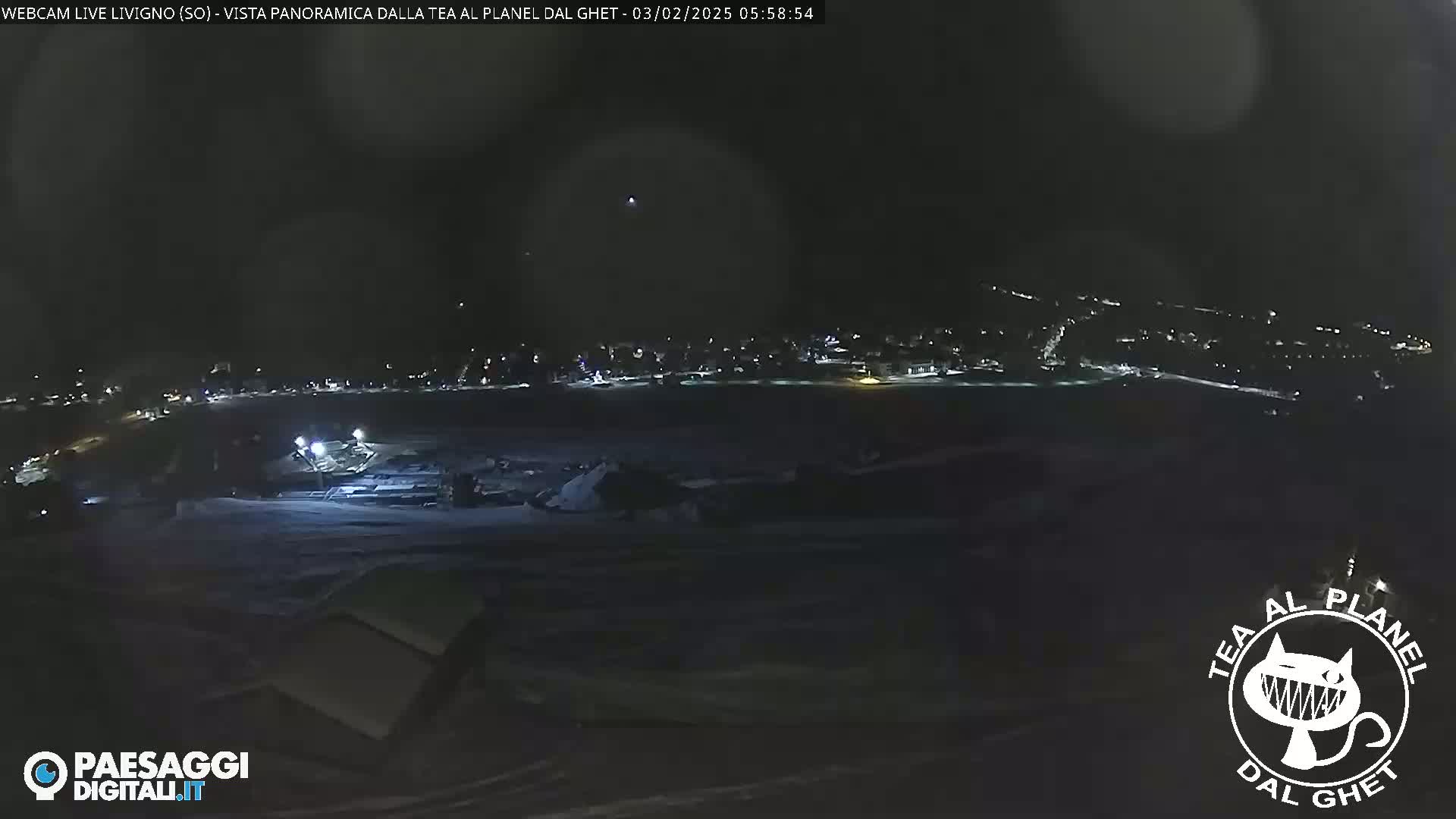 A nighttime, panoramic view of a snow-covered landscape with a distant town illuminated by lights.