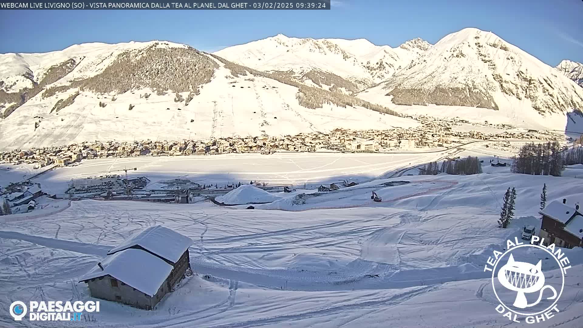 A snow-covered village nestled in a valley between snow-capped mountains under a sunny sky.