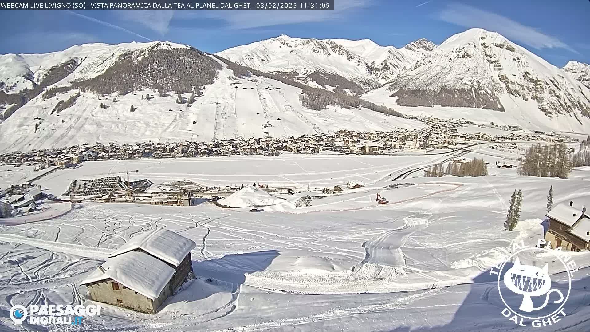 A snow-covered village nestled in a valley between snow-capped mountains on a sunny day.