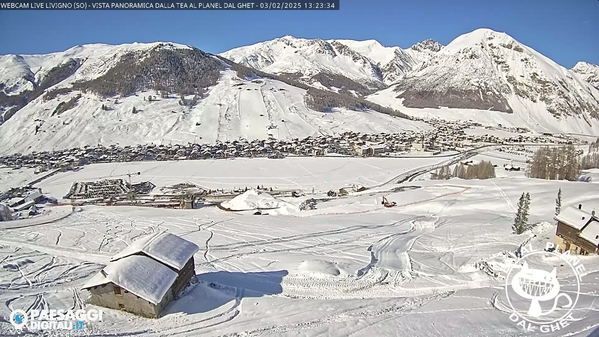 A snow-covered village nestled in a valley between snow-capped mountains on a sunny day.
