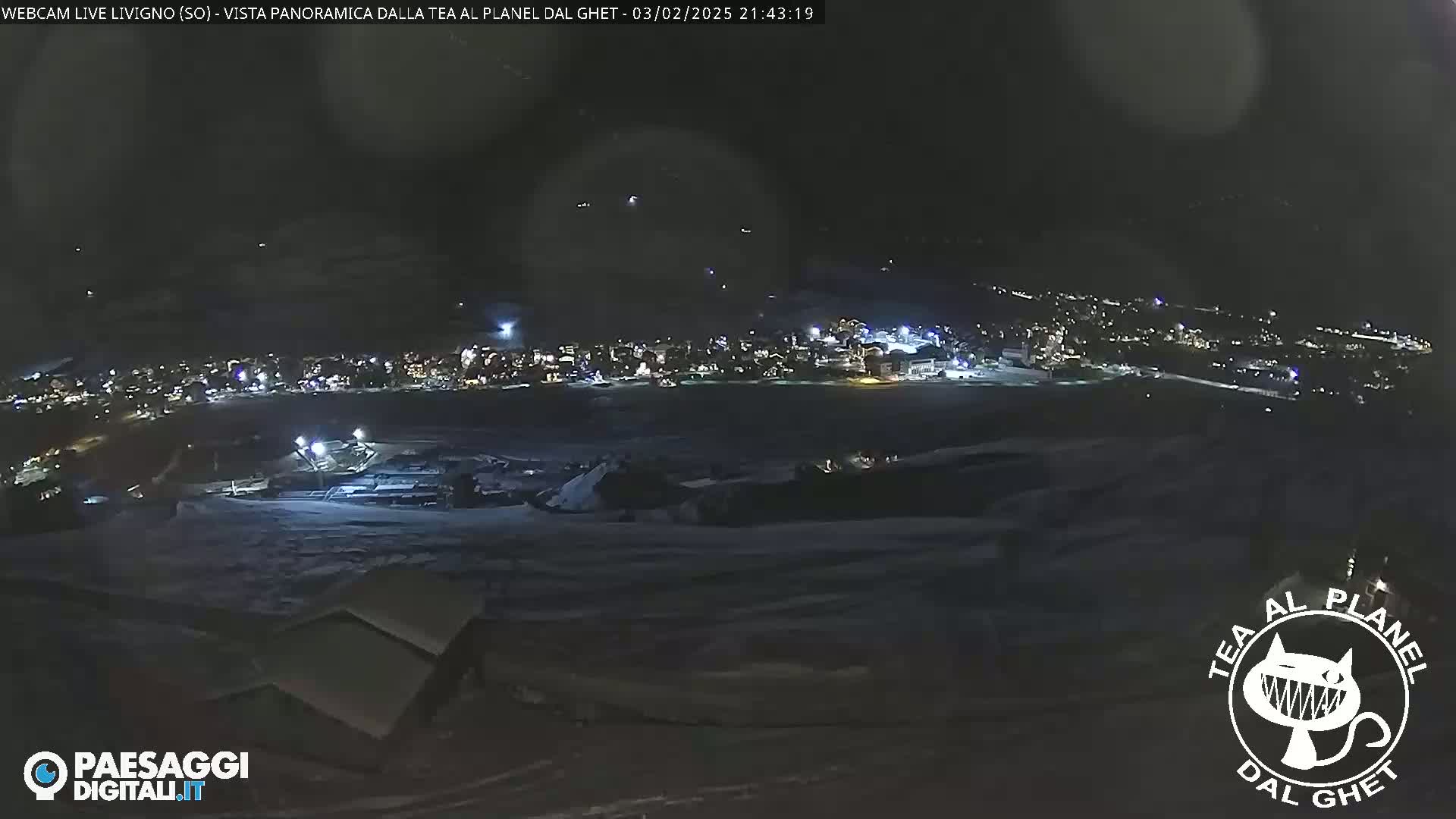 A nighttime, panoramic view of a snow-covered town illuminated by lights, with a dark, possibly cloudy sky above.