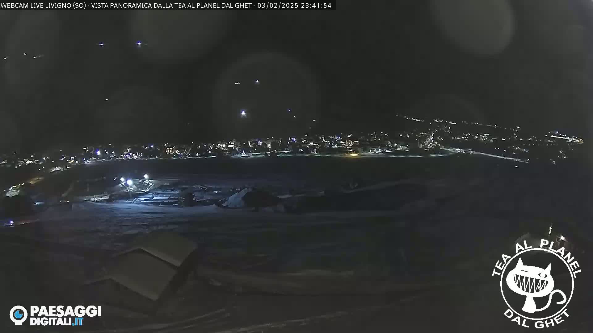 A nighttime, snowy panoramic view of a town with scattered lights, illuminated by faint lights in the sky.