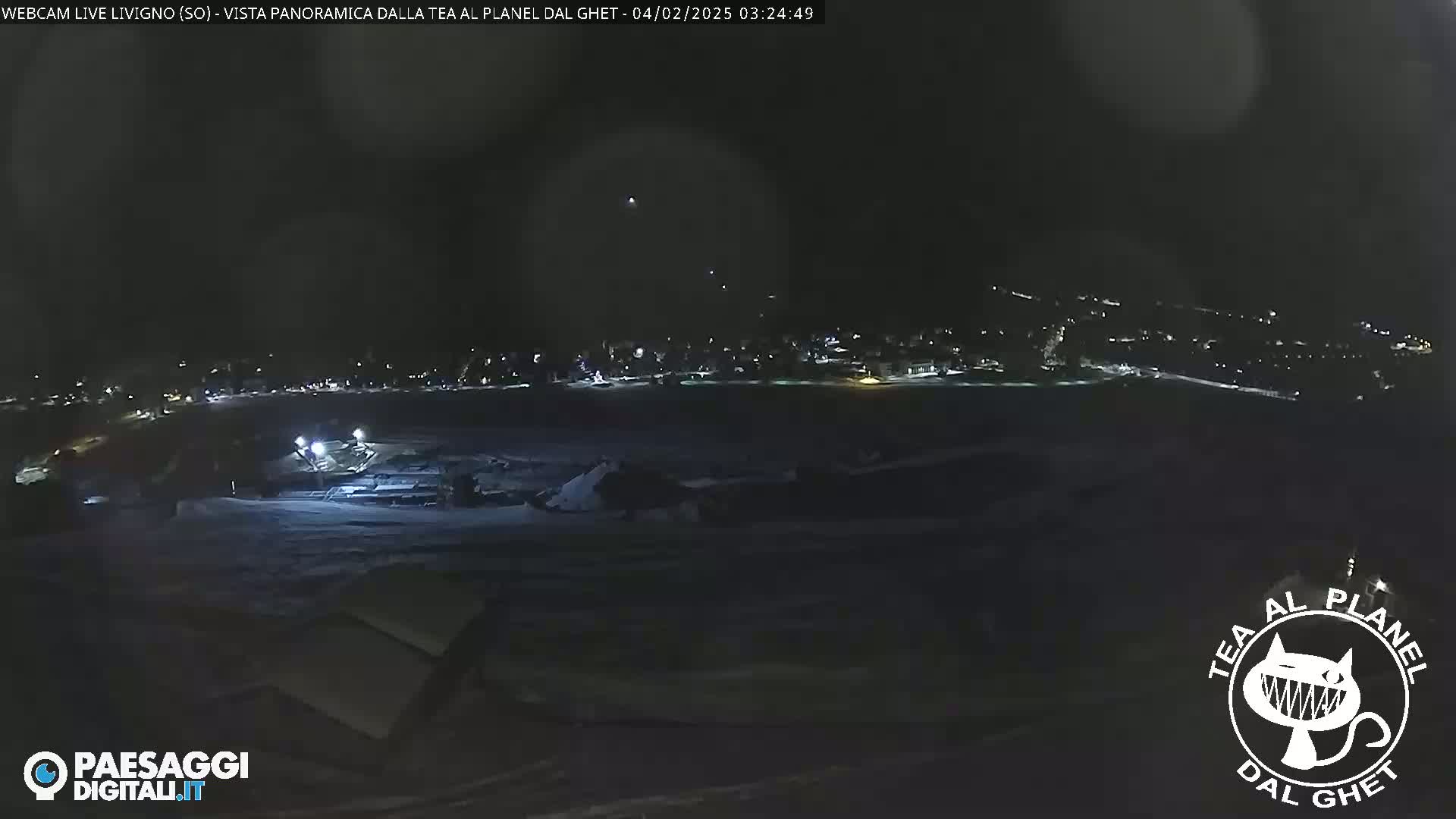 A nighttime, long shot of a snow-covered landscape with a town's lights visible in the distance.