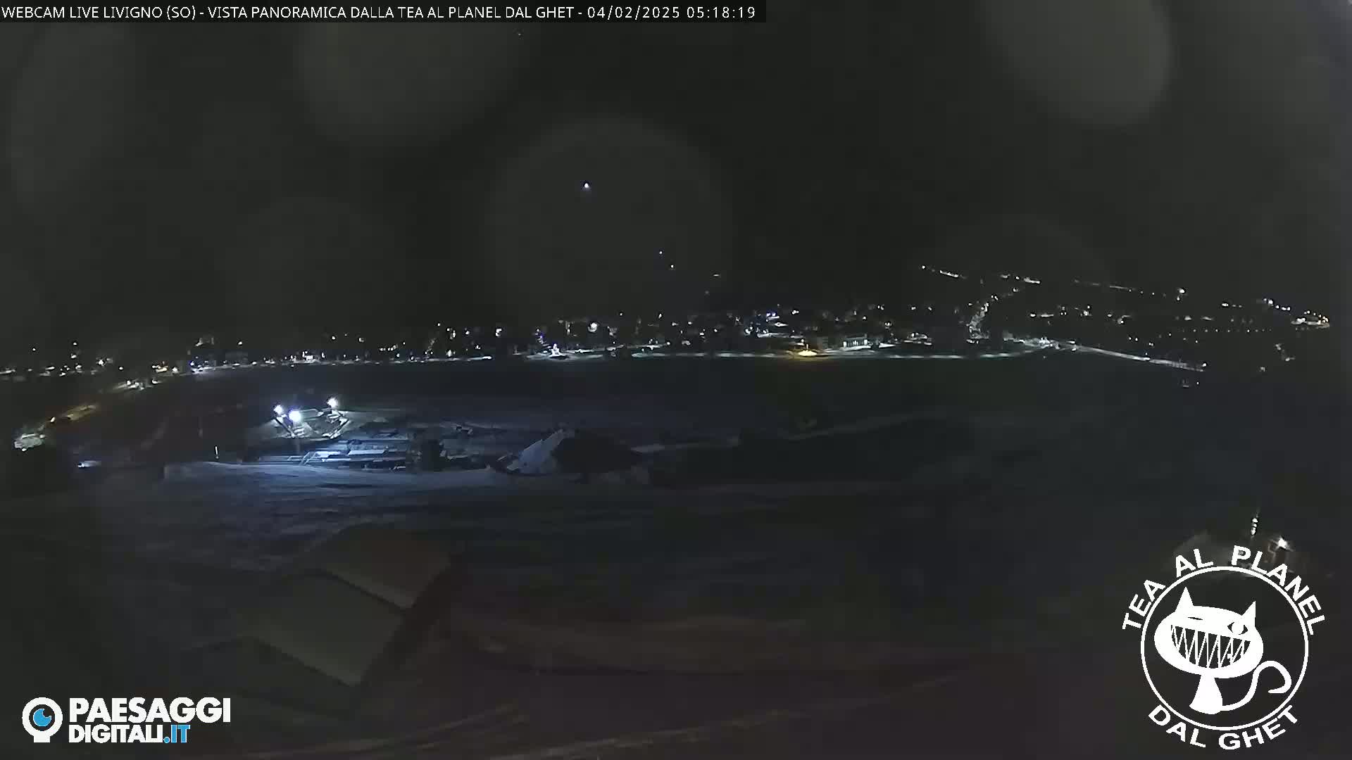 A nighttime, panoramic view of a snow-covered town, illuminated by scattered lights under a dark sky.