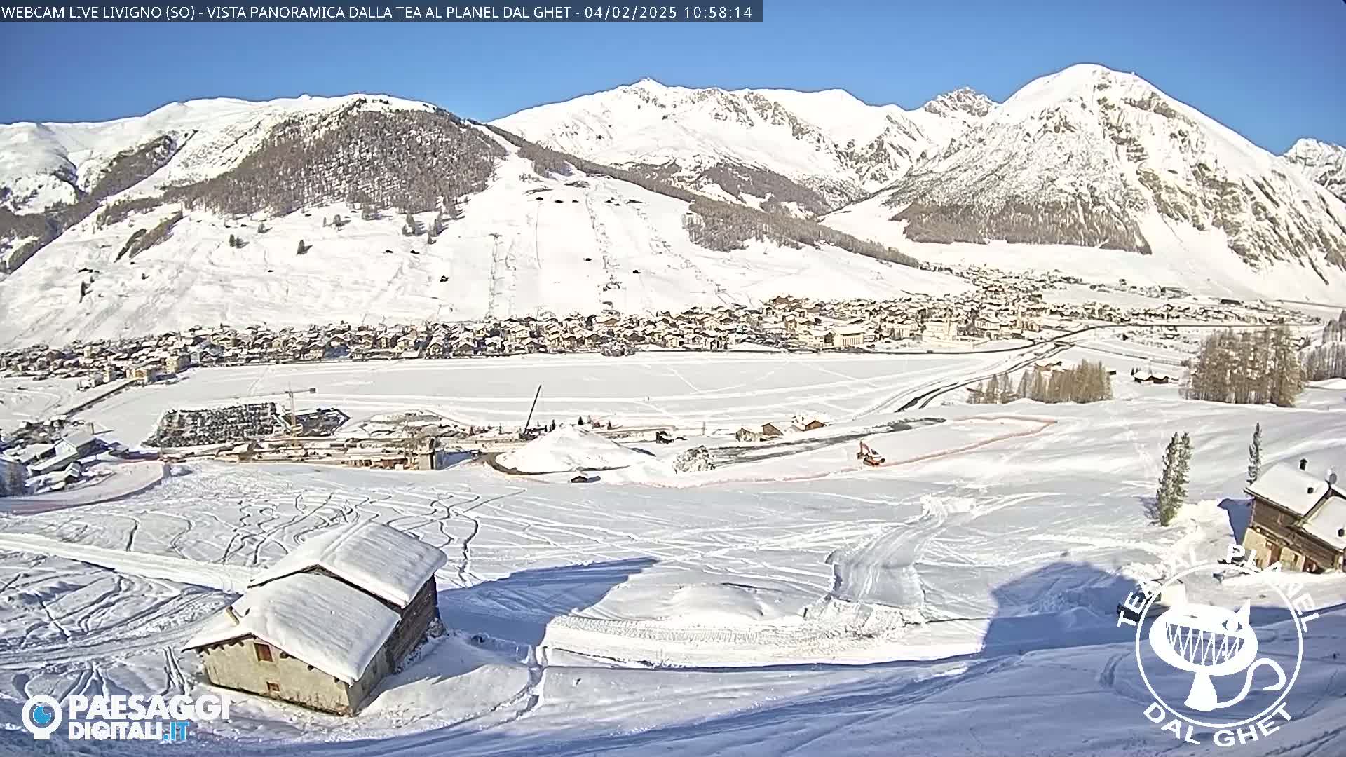 A snow-covered village nestled in a valley between snow-capped mountains under a clear, sunny sky.