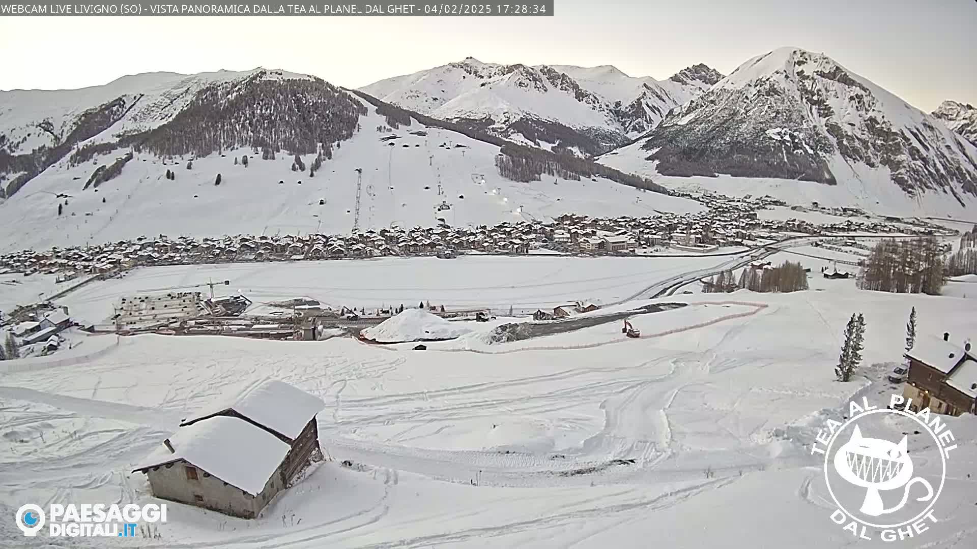 A snow-covered village nestled in a valley between snow-capped mountains under an overcast sky.