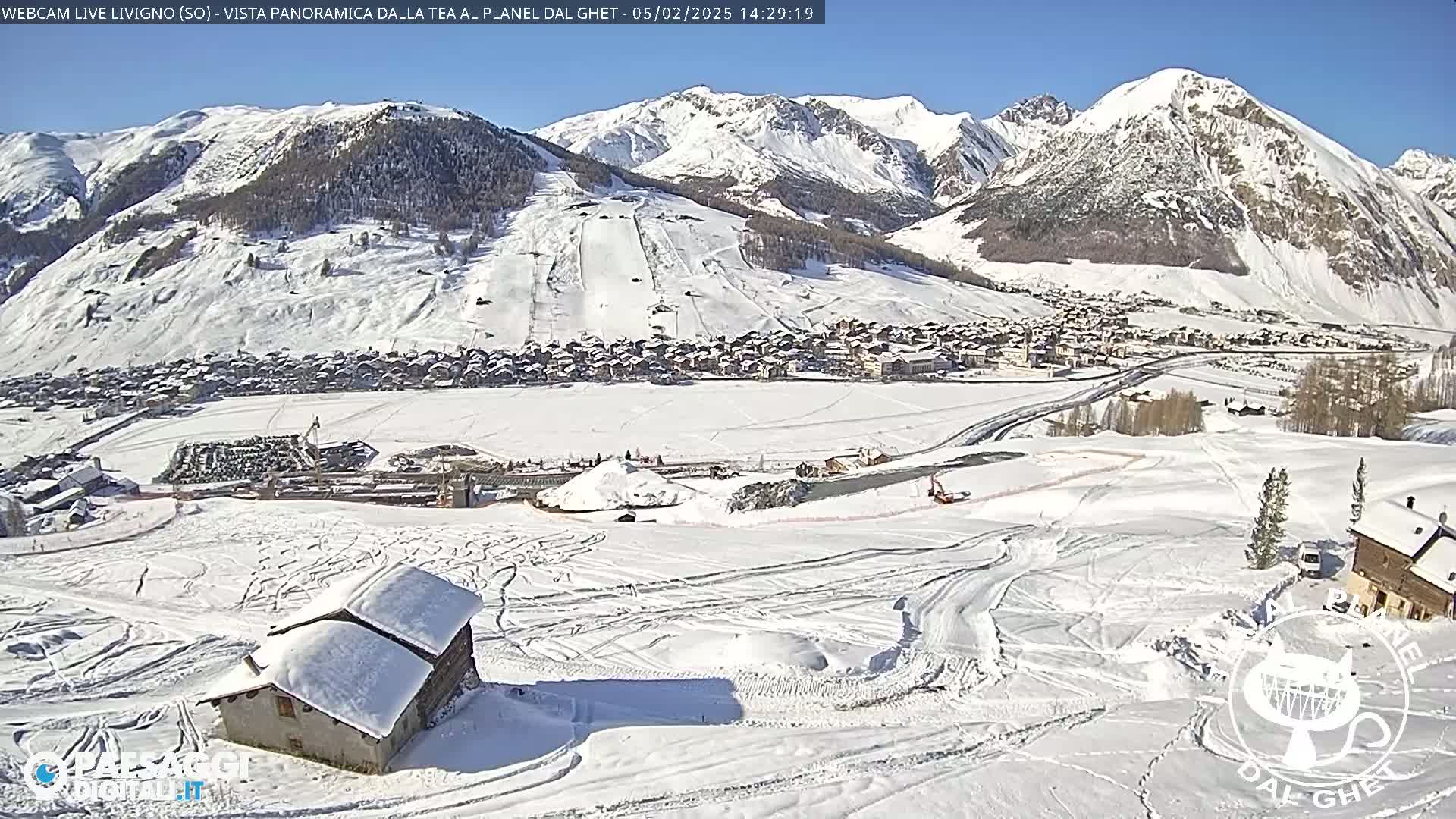 A snow-covered mountain village nestled in a valley, with ski runs visible on the surrounding slopes, under a clear blue sky.