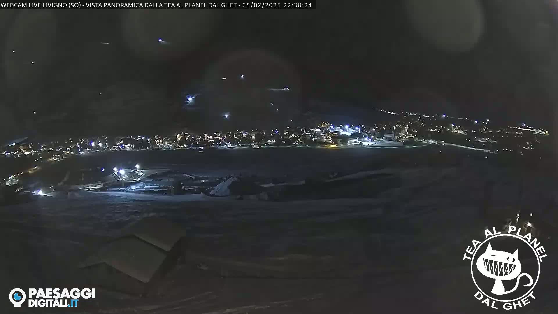 A nighttime, panoramic view of a snow-covered town with scattered lights, under a clear, dark sky.