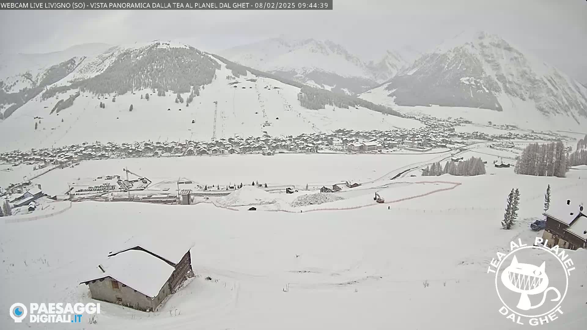 A snow-covered village nestled in a valley between snow-dusted mountains under an overcast sky.