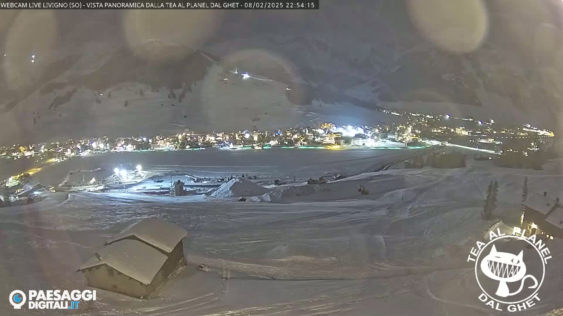 A snow-covered landscape at night, showing a town illuminated below and a small snow-covered building in the foreground.