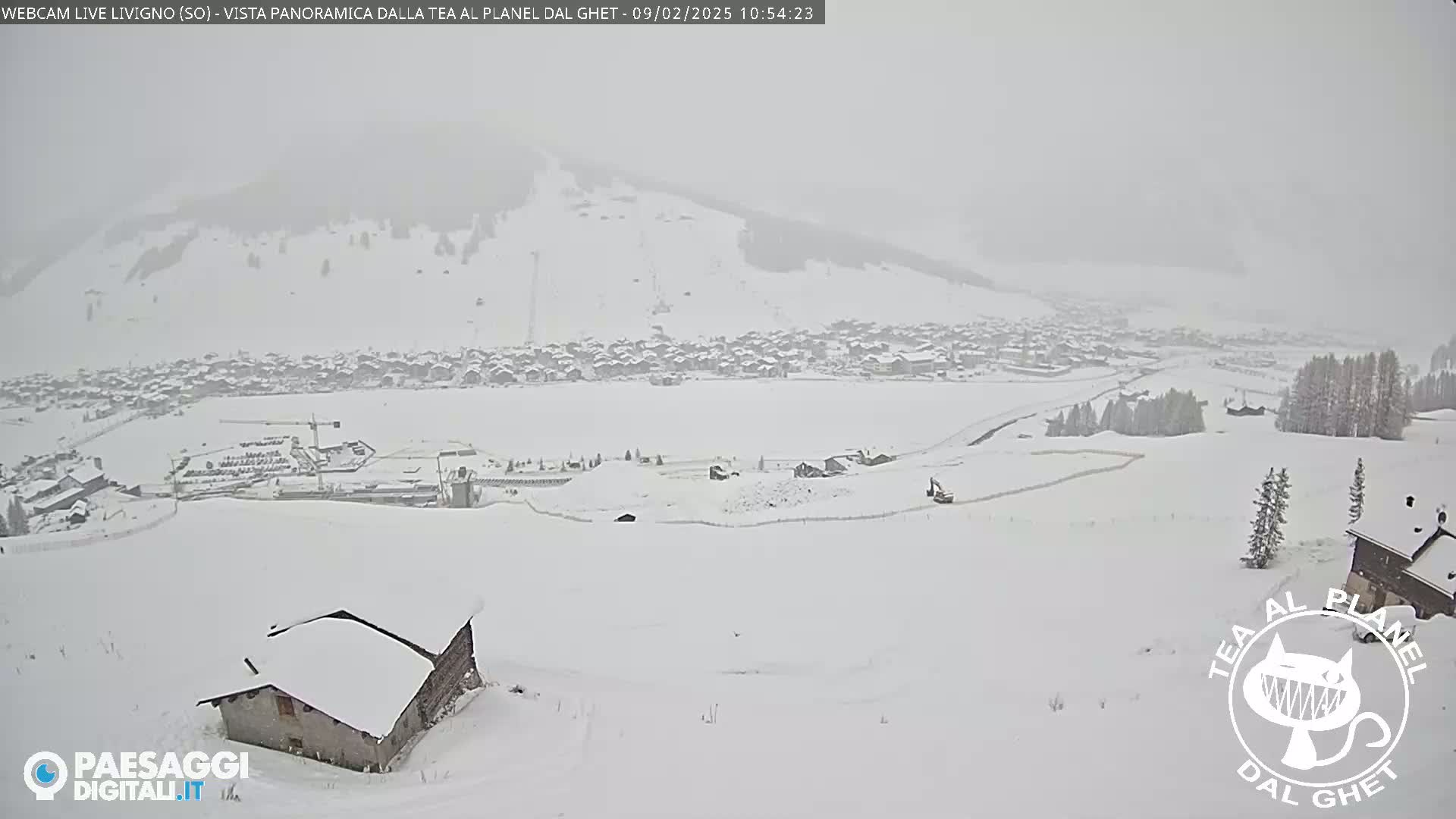 A snow-covered mountain village is visible under heavy snowfall, with a few buildings and some construction equipment in the foreground.