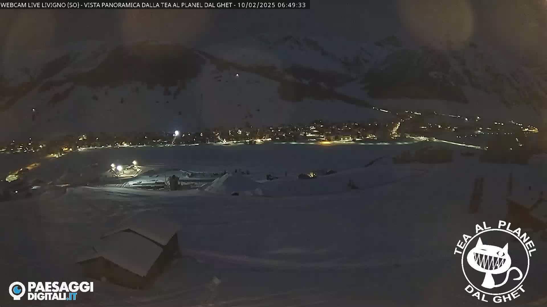 A nighttime, snow-covered landscape shows a village with lights below a dark mountain.