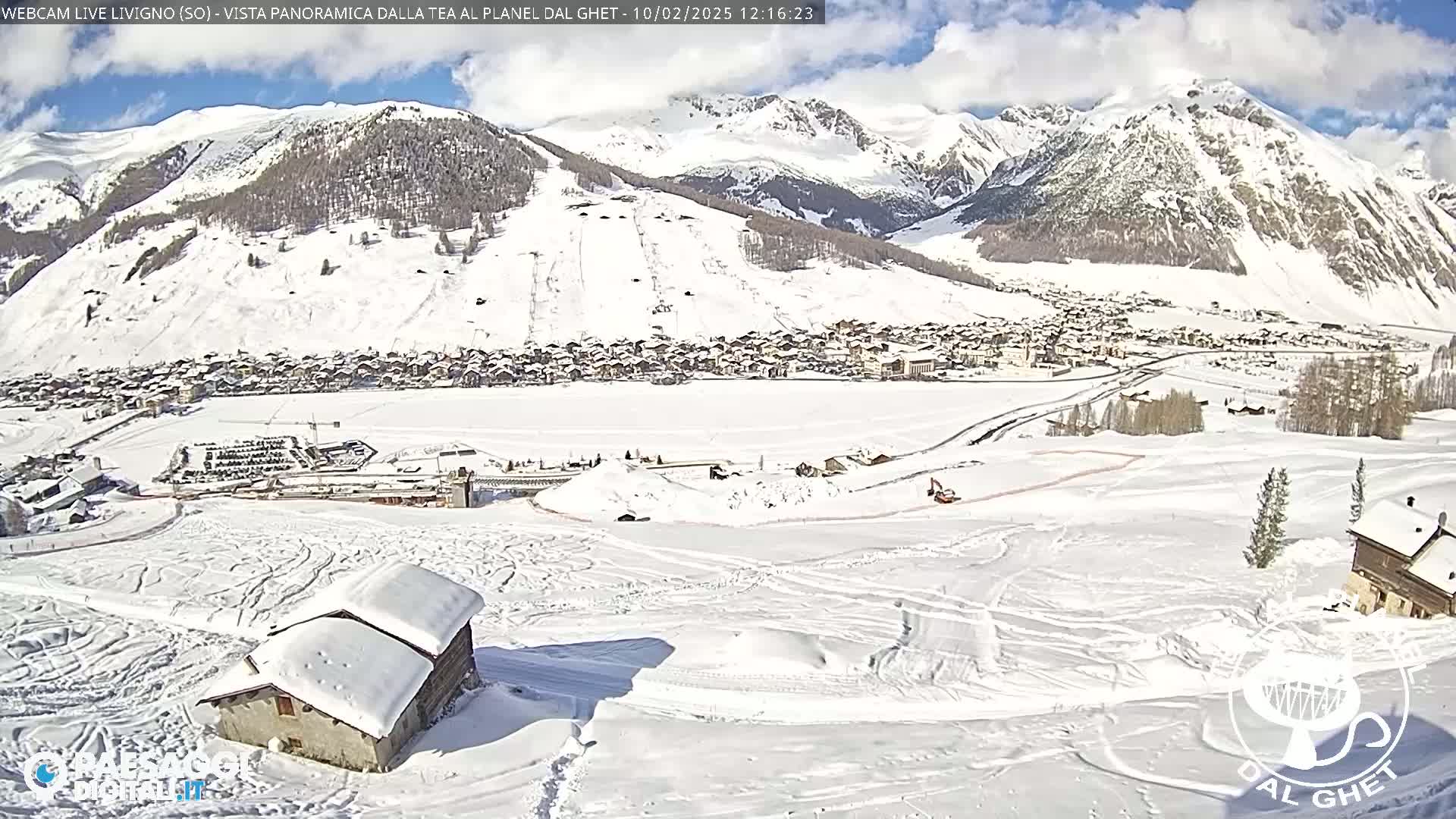 A snow-covered mountain village is visible beneath a mostly sunny sky, with snow-covered hills and mountains in the background.