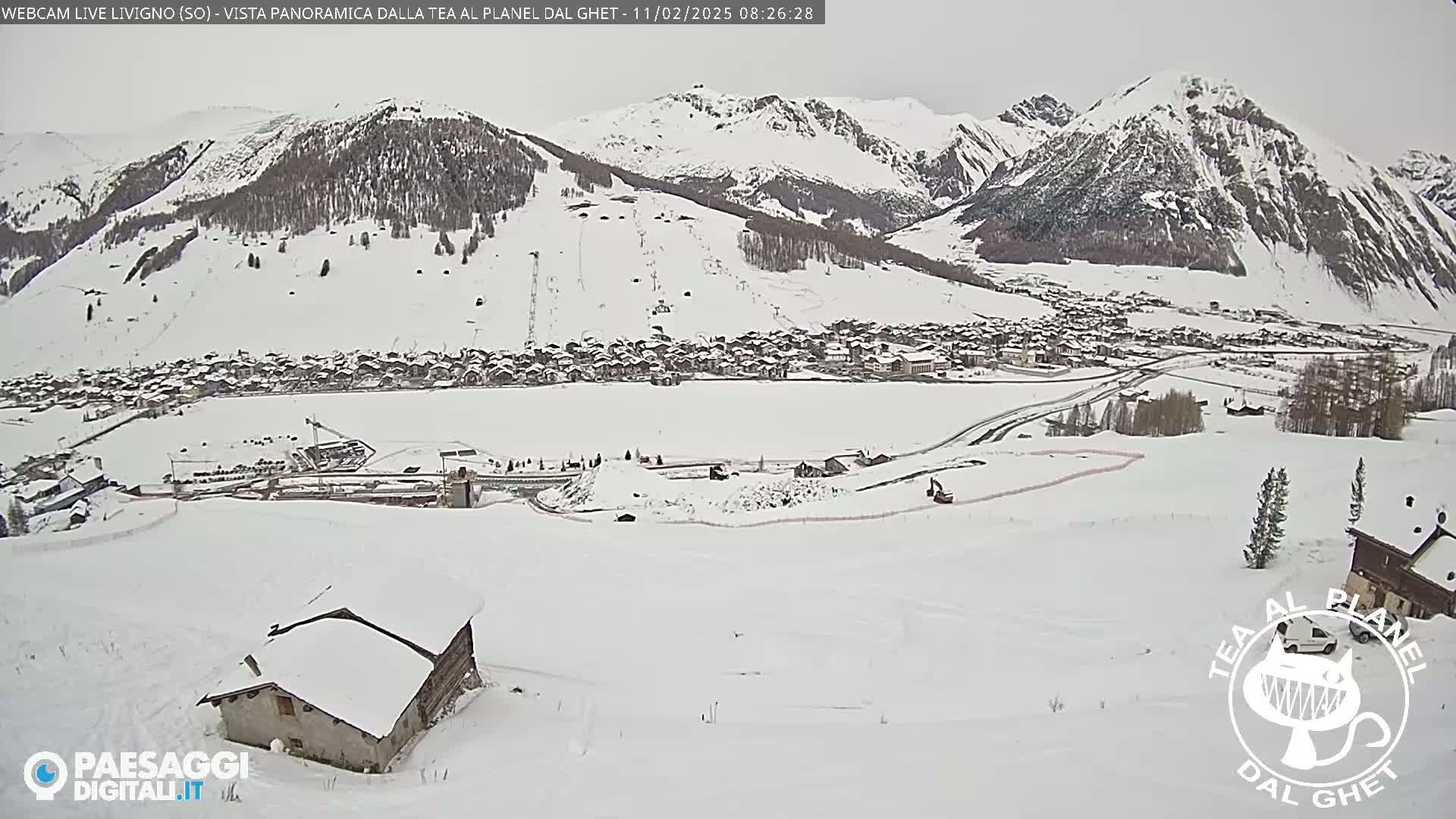 A snow-covered village nestled in a valley between snow-capped mountains under an overcast sky.
