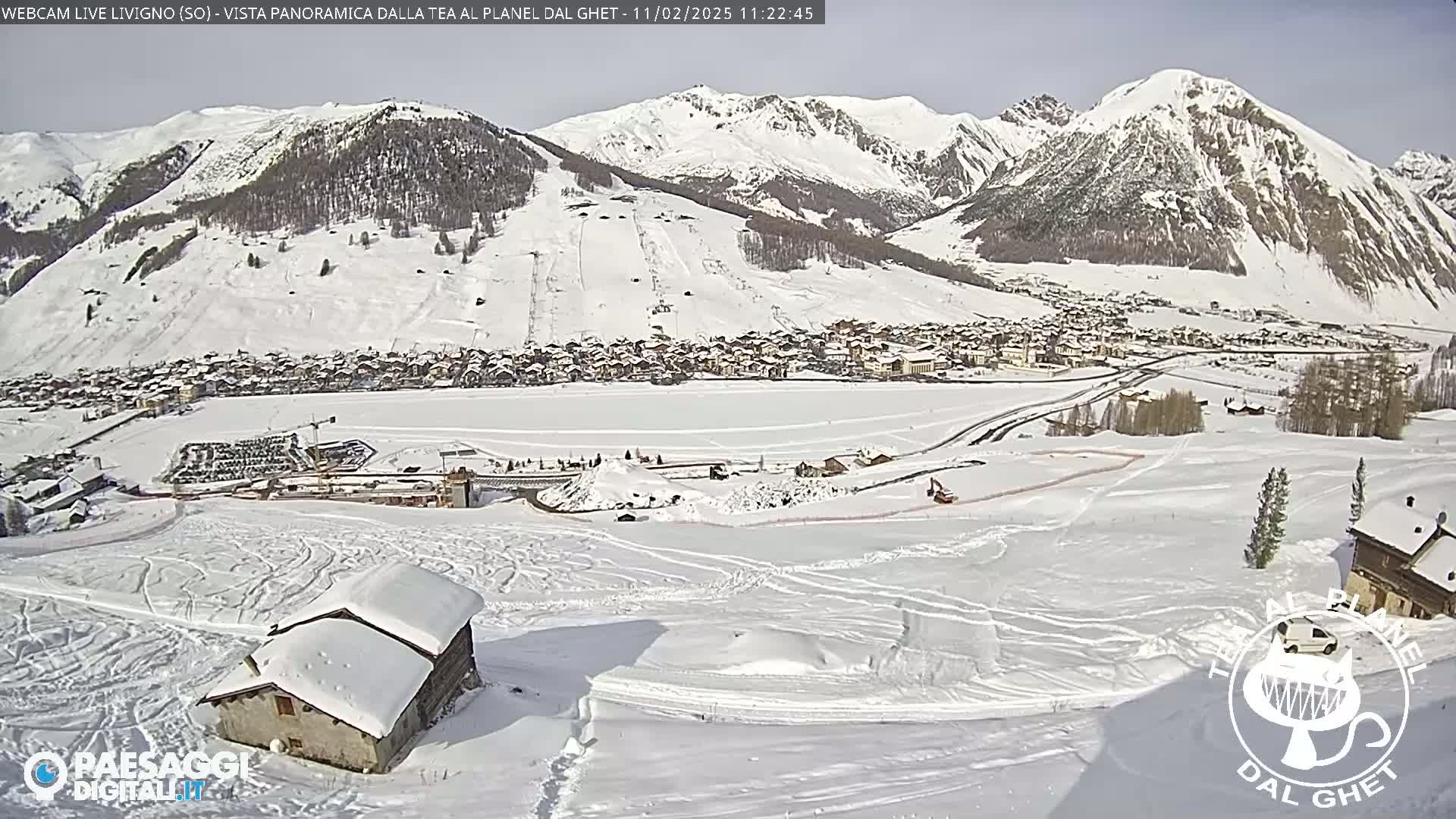 A snow-covered mountain village is nestled in a valley beneath snow-capped mountains on a sunny day.