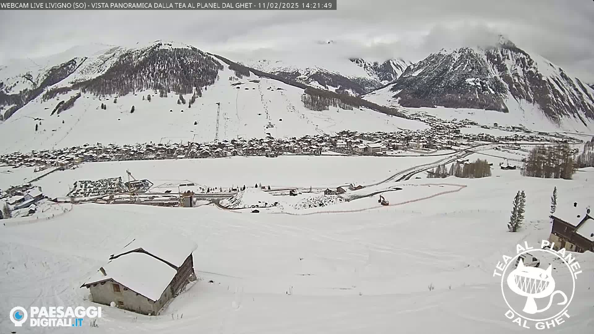 A snow-covered village nestled in a valley between snow-capped mountains under an overcast sky.