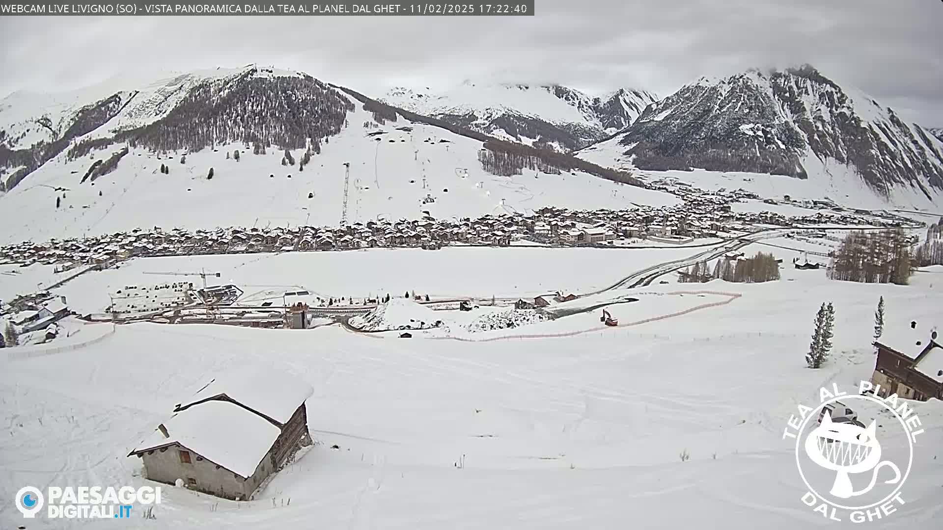 A snow-covered village nestled in a valley between snow-capped mountains under an overcast sky.