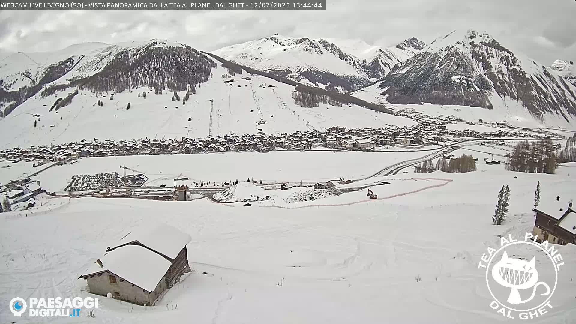 A snow-covered village nestled in a valley between snow-capped mountains on an overcast day.