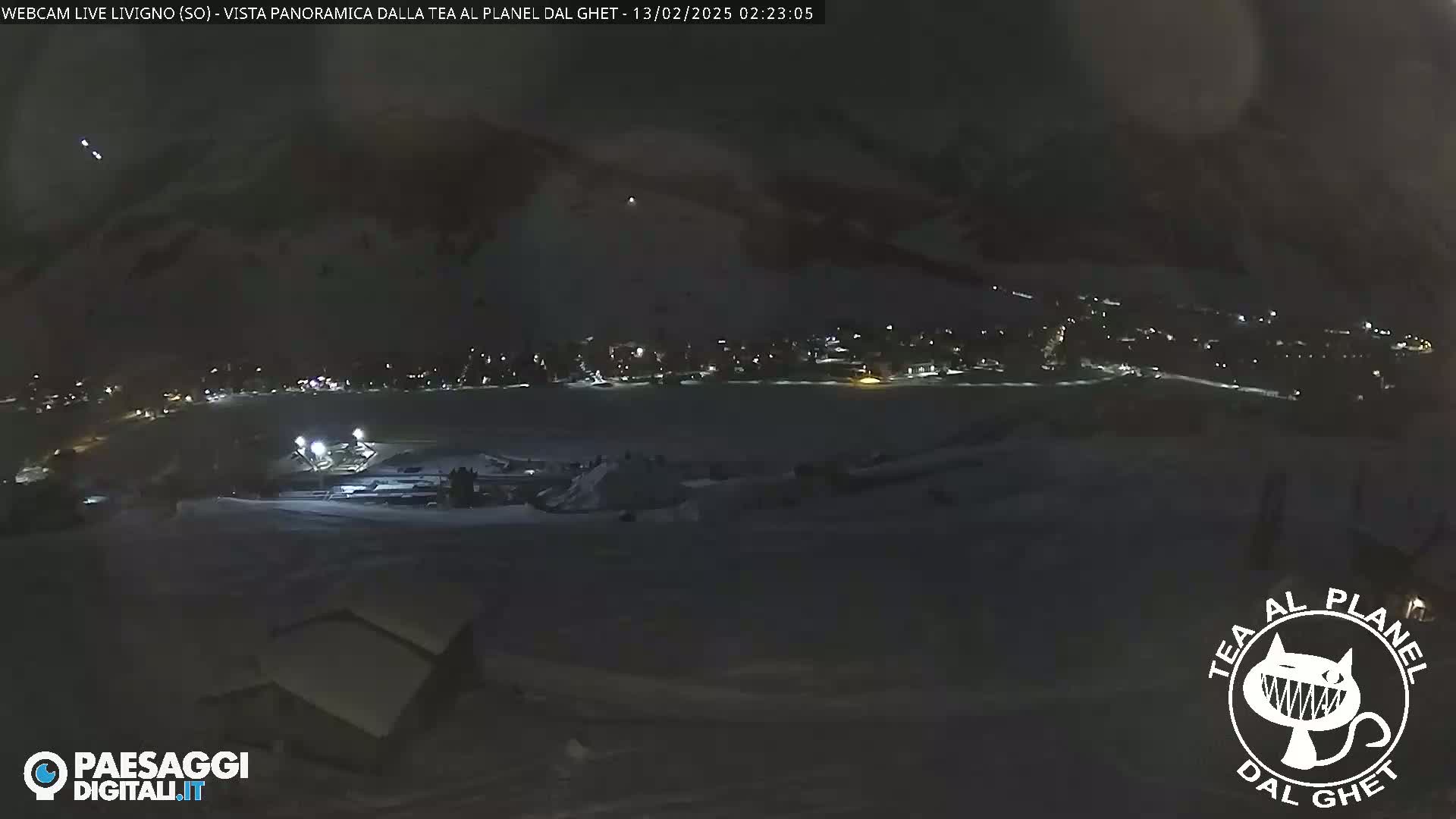A nighttime, snow-covered landscape shows a dimly lit town in the distance under a dark sky.