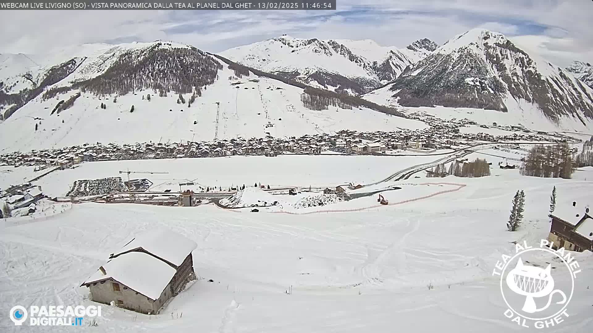 A snow-covered village nestled in a valley between snow-capped mountains under a cloudy sky.