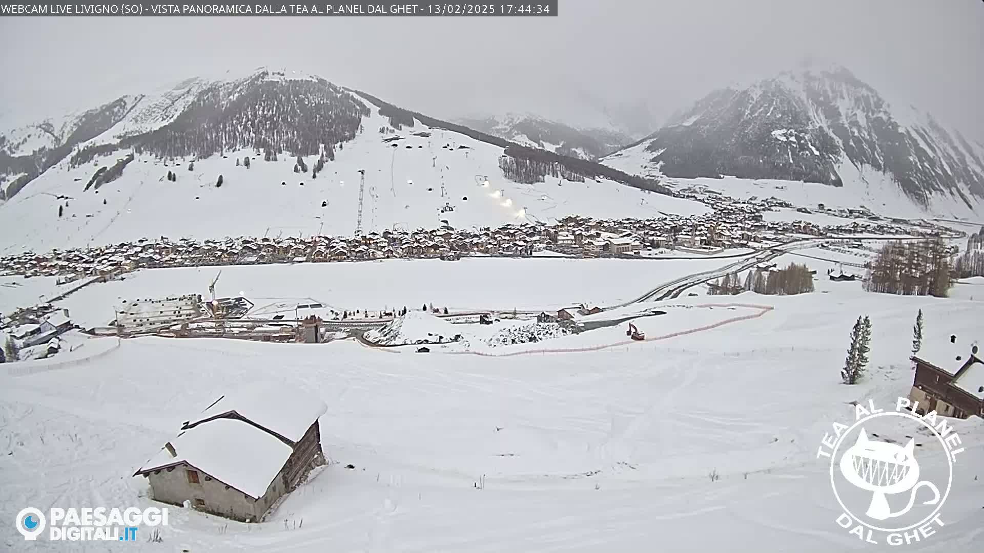 A snow-covered village nestled in a valley between snow-capped mountains under an overcast sky.