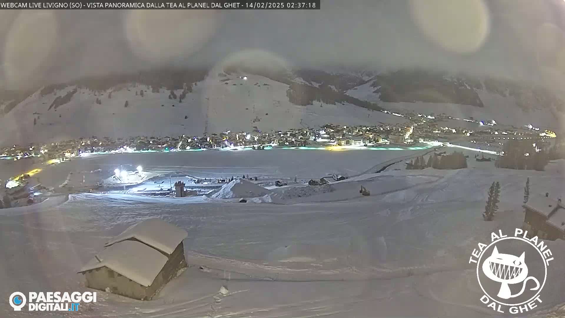 A snow-covered mountain village at night is seen from a high vantage point, under a cloudy sky.