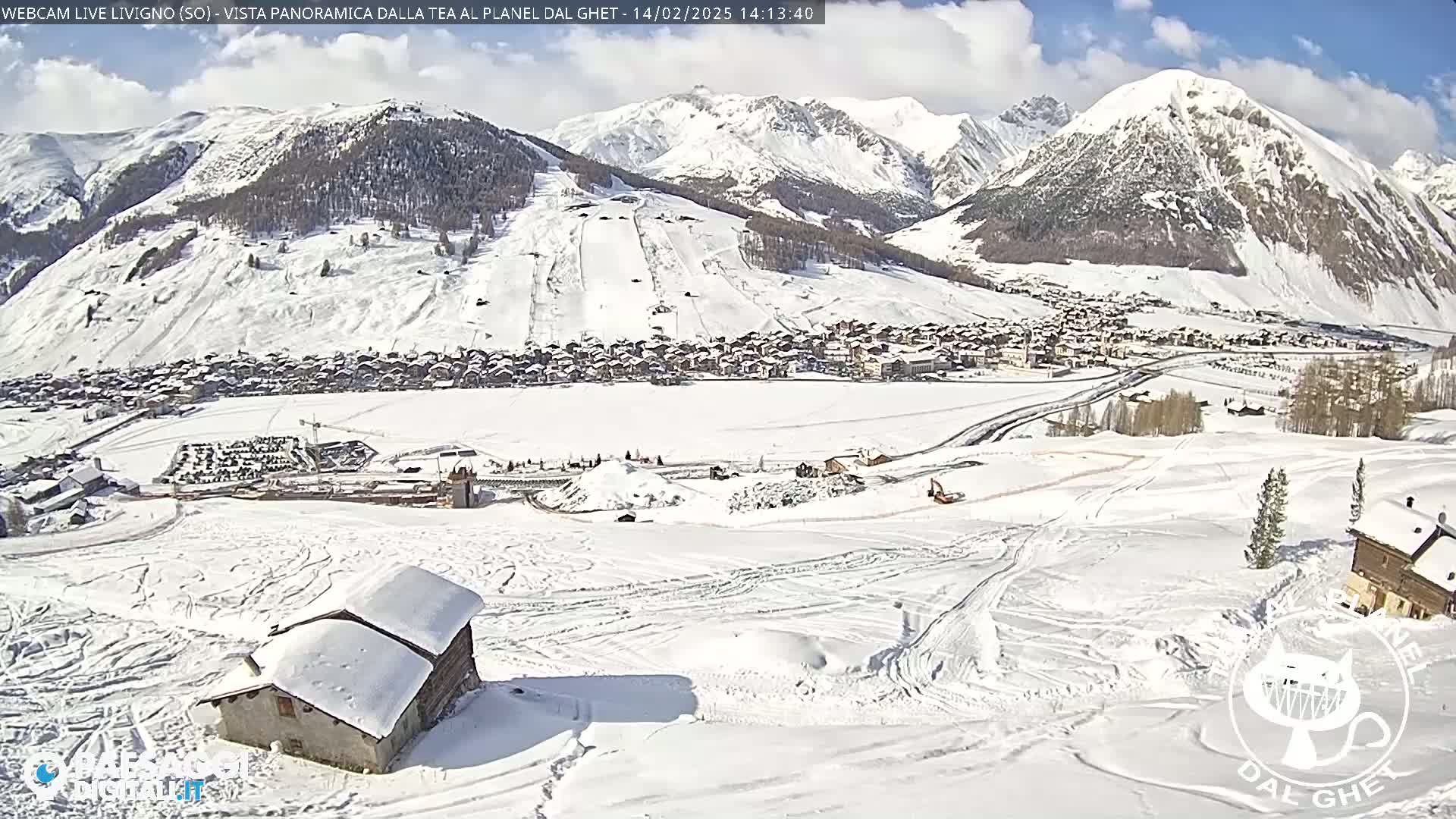 A snow-covered mountain valley town is visible under a partly sunny sky, with snow-covered hills and mountains in the background.