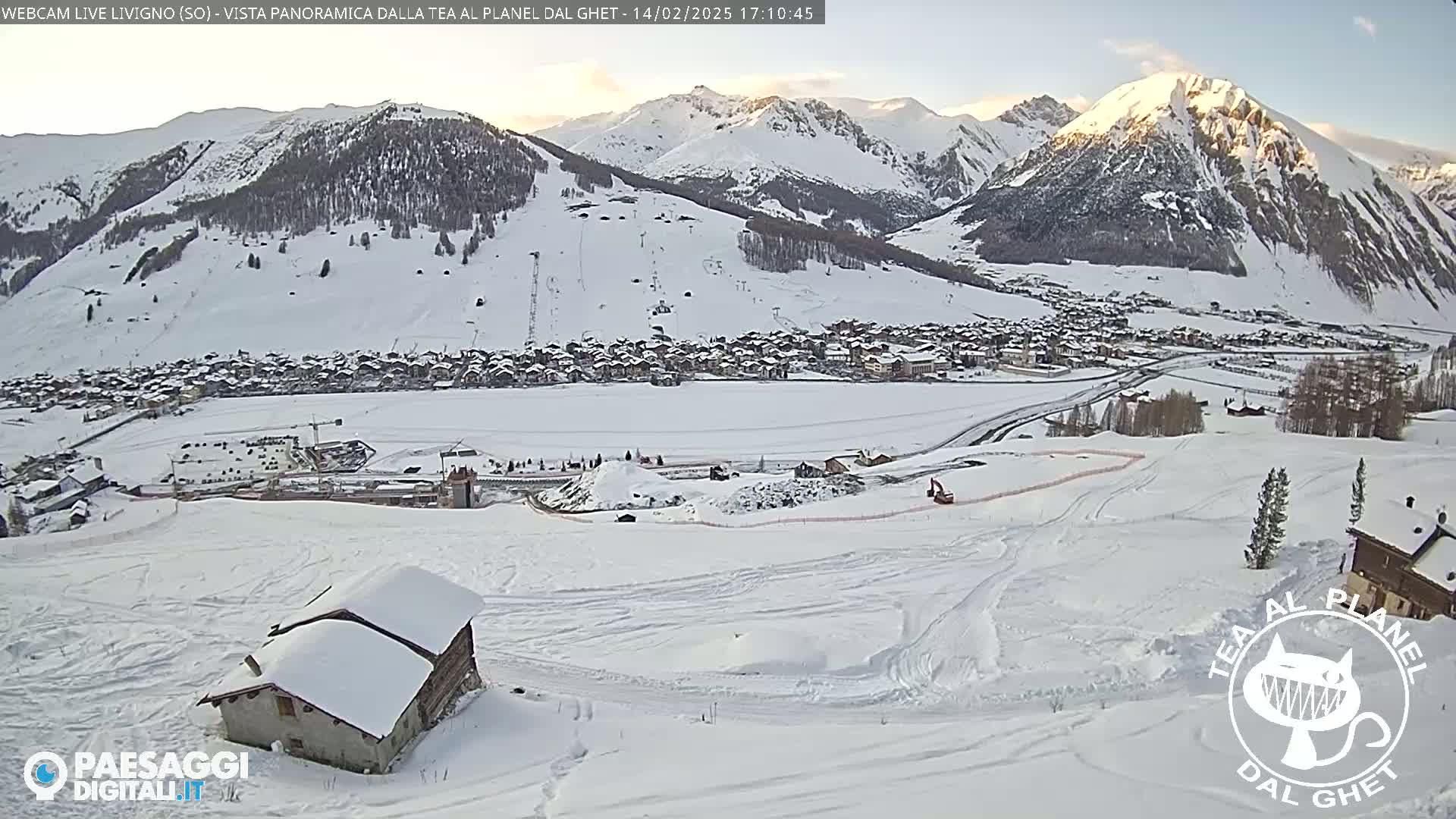 A snow-covered mountain village is nestled in a valley beneath snow-capped mountains on a sunny day.
