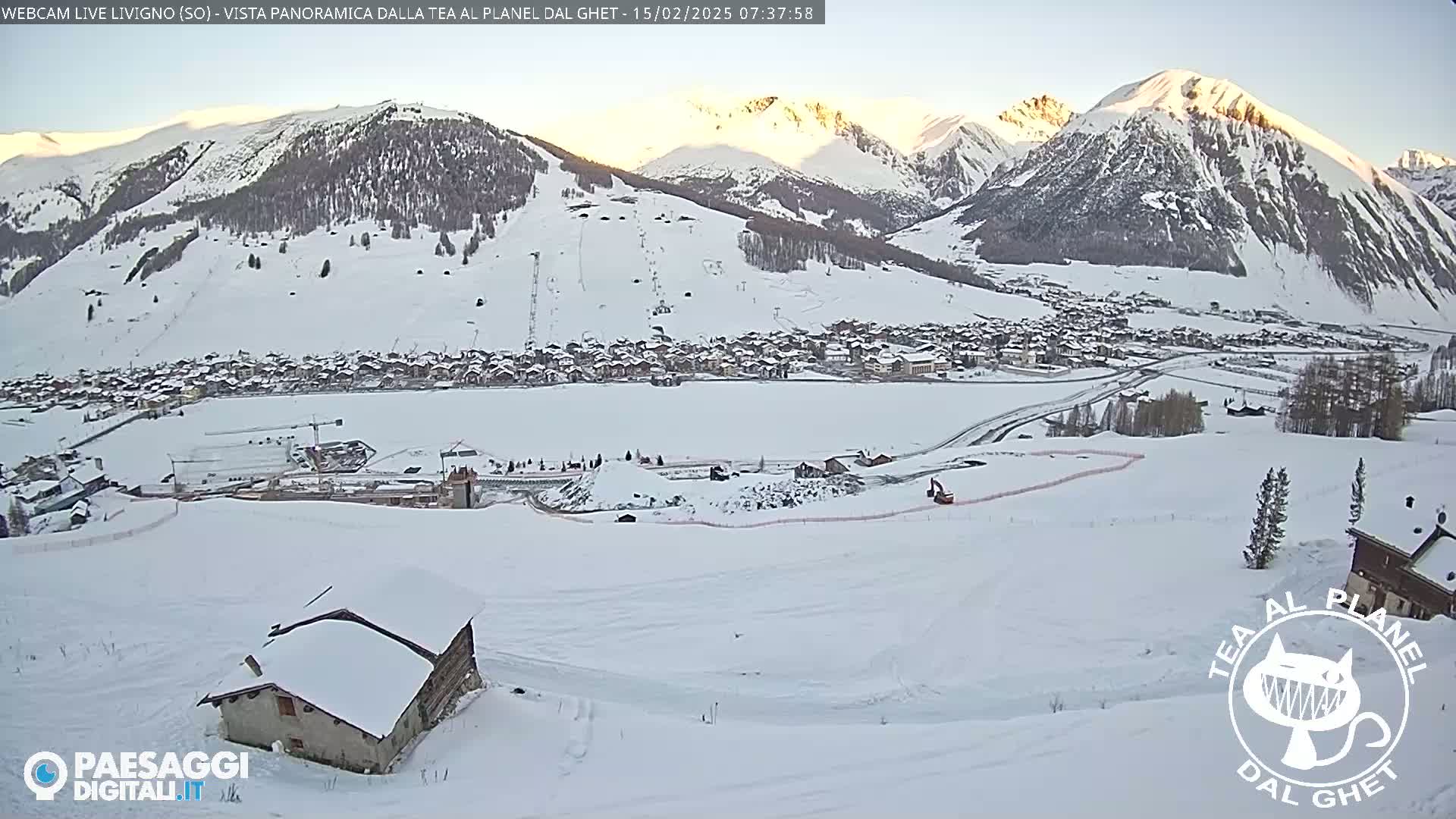 A snow-covered village nestled in a valley between sunlit mountains, with a small snow-covered house in the foreground.