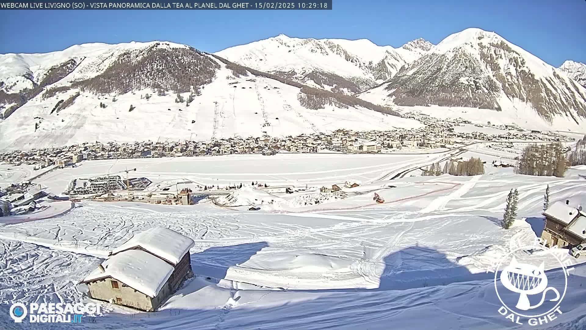 A snow-covered mountain village is nestled in a valley beneath snow-capped mountains on a sunny day.