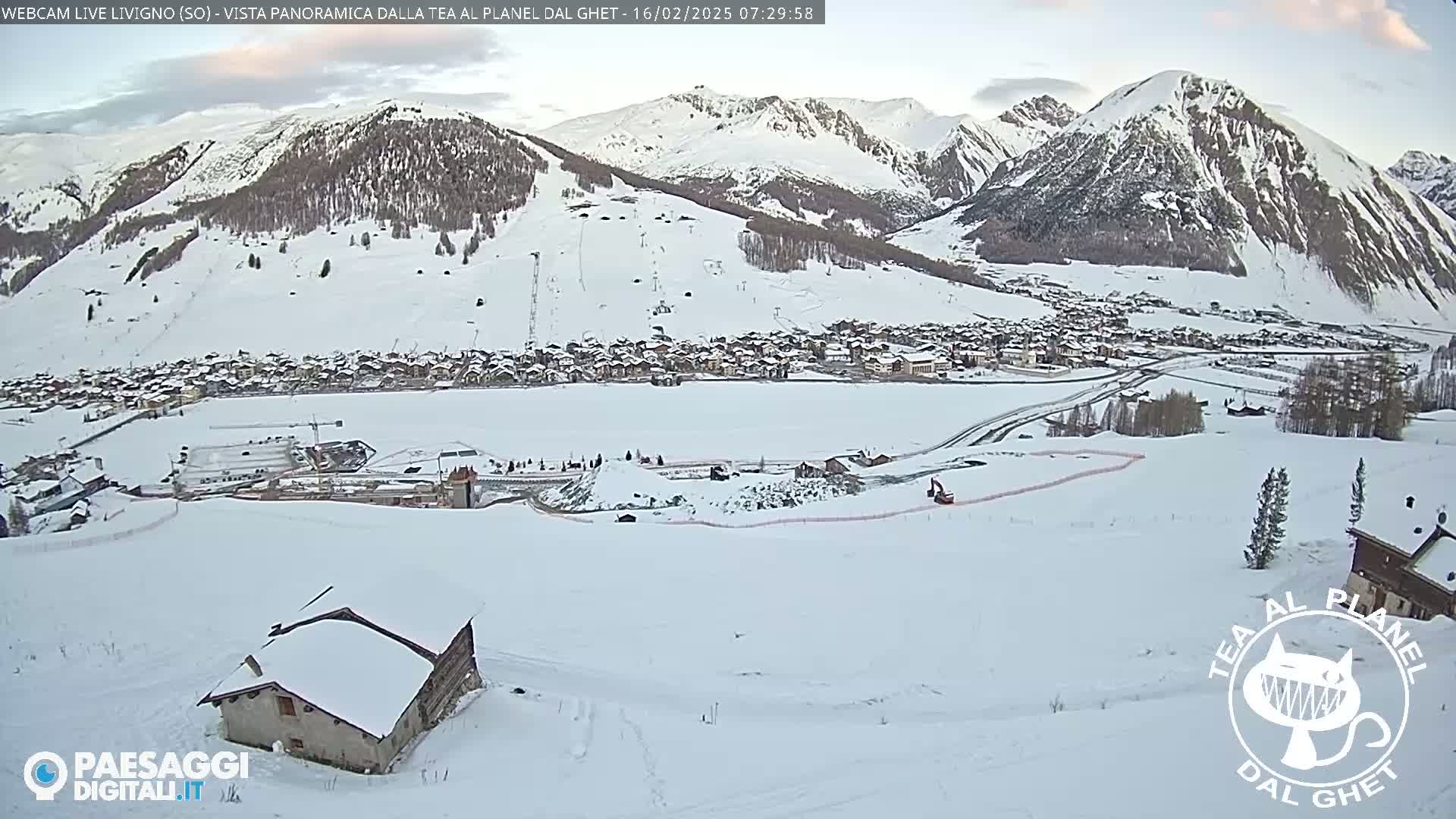 A snow-covered village nestled in a valley between snow-capped mountains under a mostly clear sky.