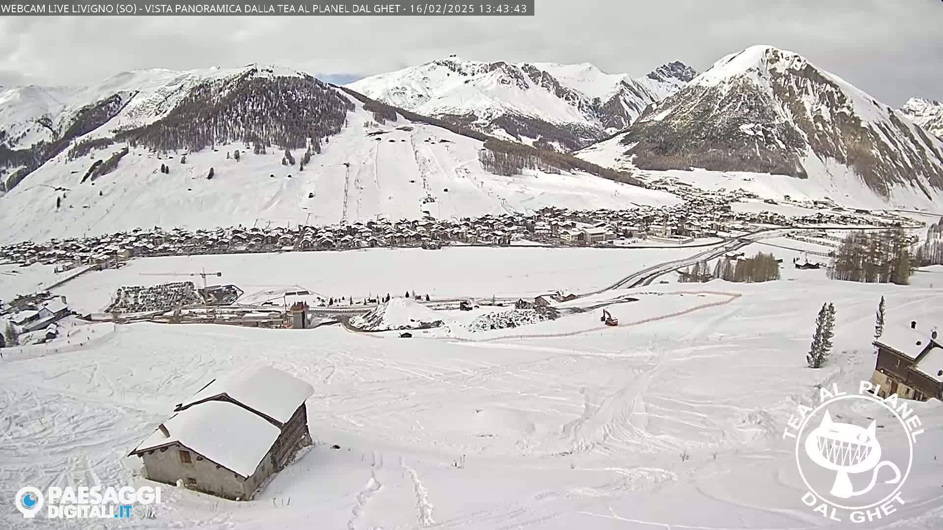A snow-covered mountain valley scene with a village nestled below, viewed from a high vantage point on an overcast day.