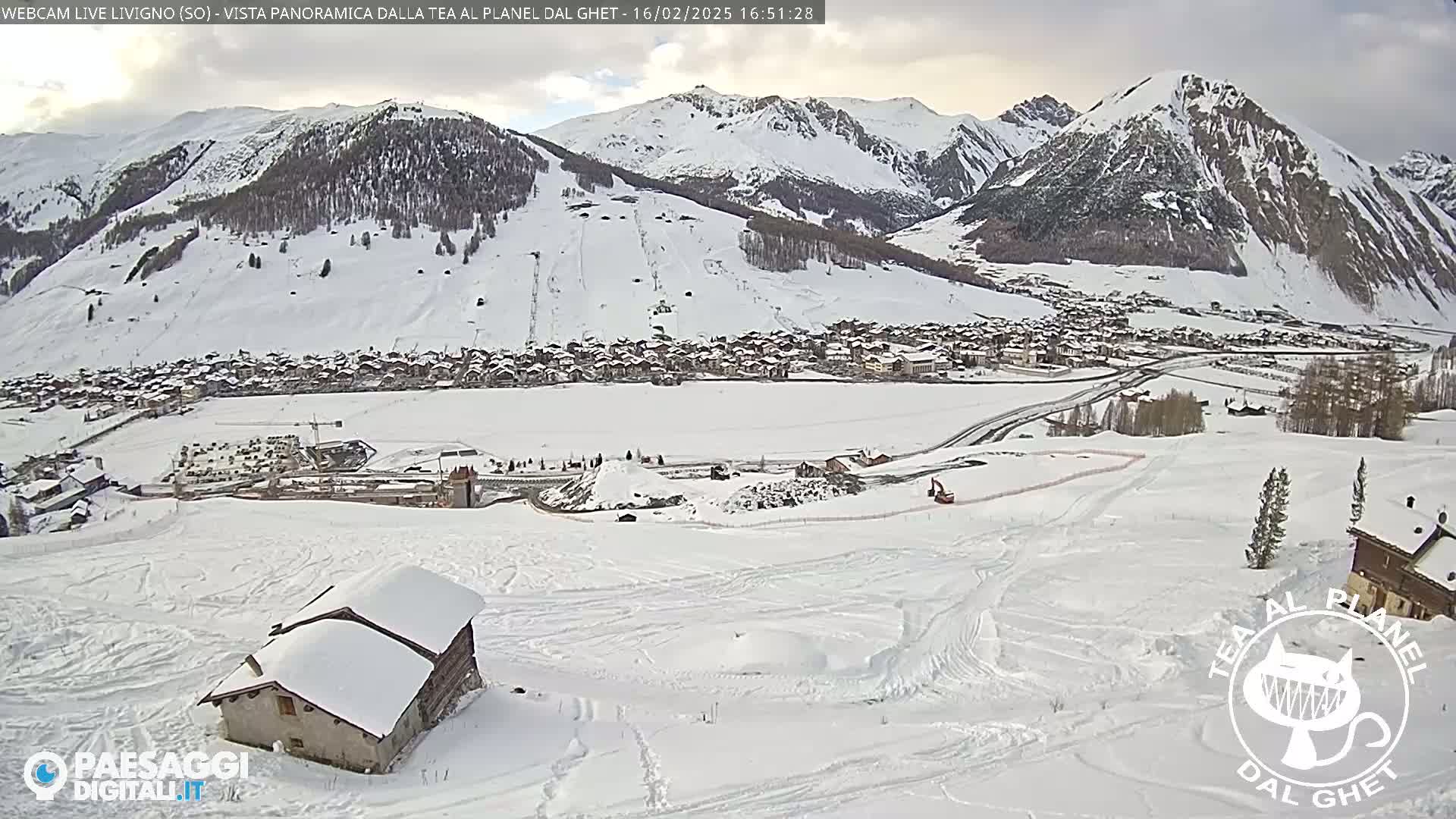 A snow-covered mountain village is nestled in a valley below snow-covered slopes, under an overcast sky.