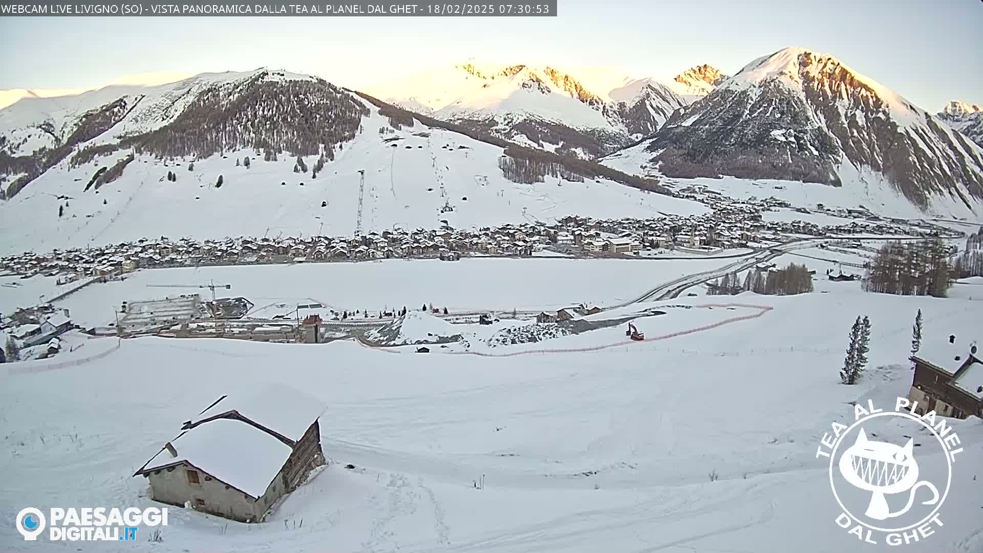 A snow-covered mountain village is visible below a sunlit mountain range, with a small snow-covered house in the foreground.