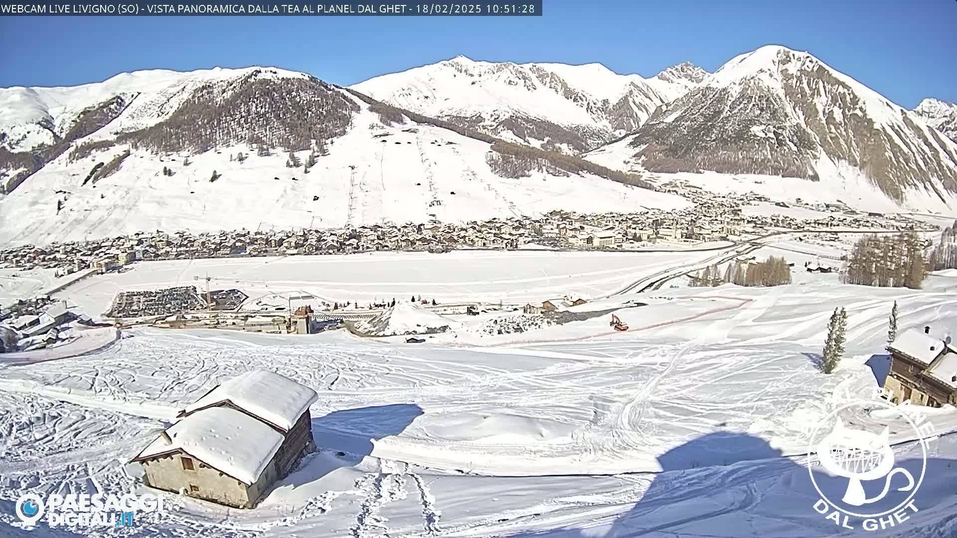 A snow-covered mountain village is nestled in a valley beneath snow-capped mountains on a sunny day.