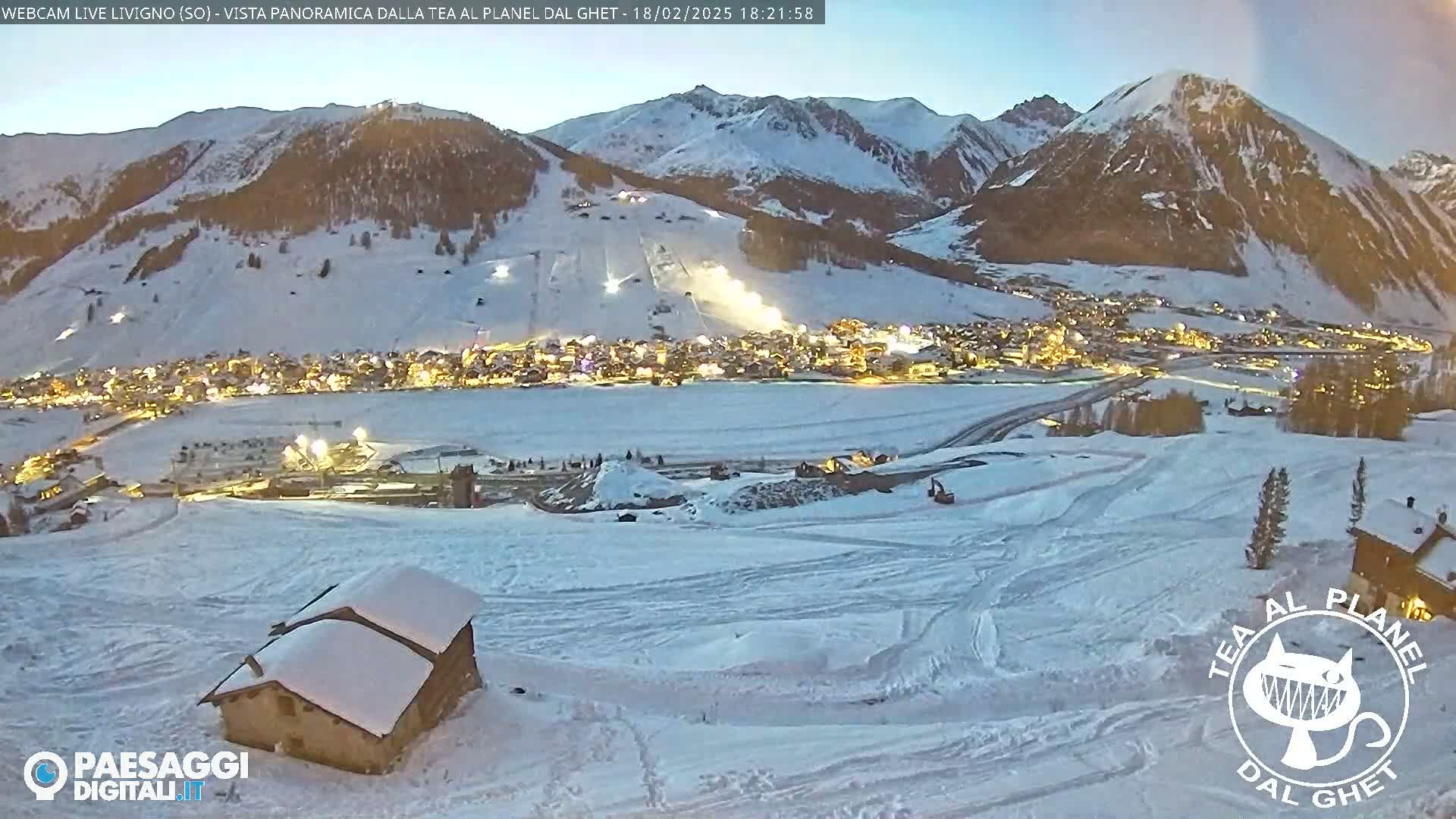 A snow-covered mountain village is illuminated at twilight, with snow-covered slopes and mountains in the background.