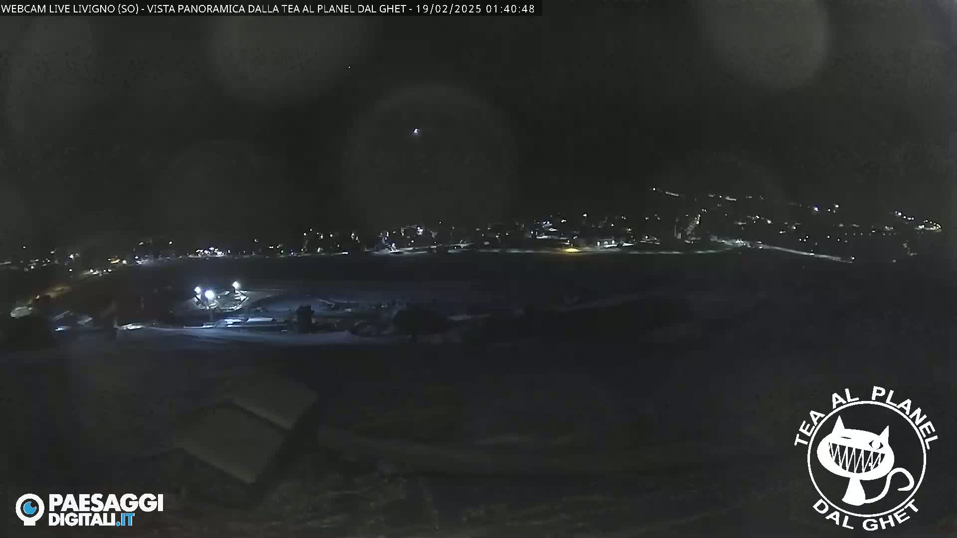 A nighttime, long shot of a snow-covered landscape with a dimly lit town in the distance.