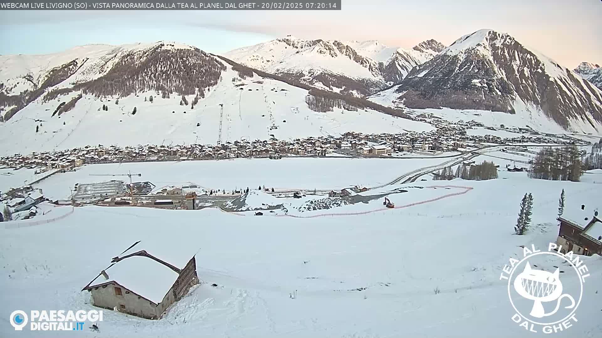 A snow-covered mountain village is nestled in a valley surrounded by snow-capped mountains under a dawn sky.