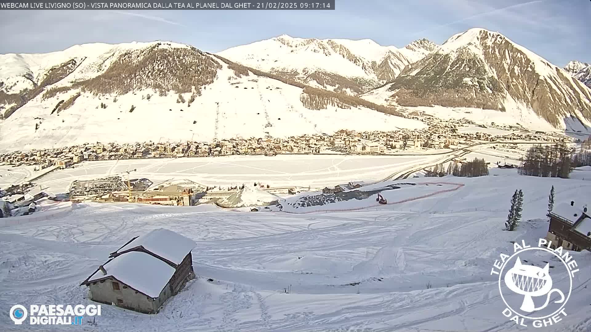 A snow-covered village nestled in a valley between snow-capped mountains under a clear, sunny sky.