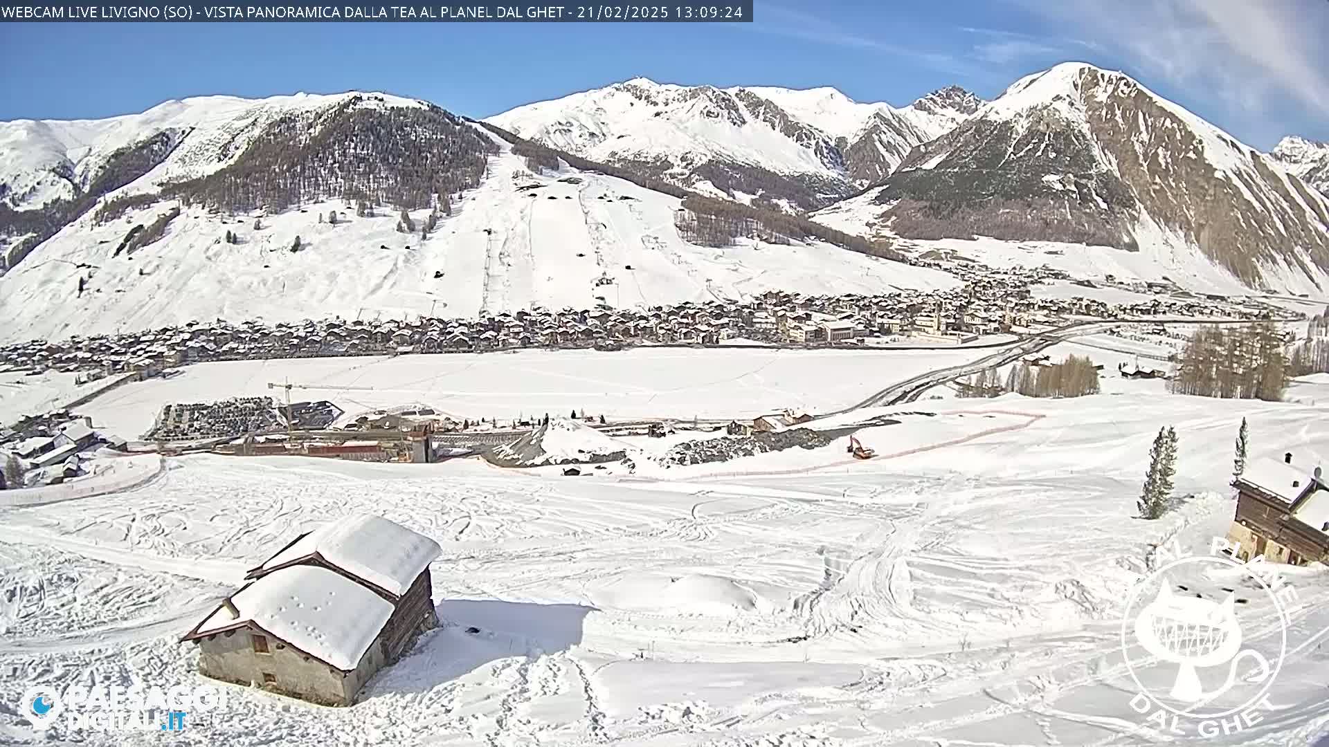 A snow-covered mountain valley town is seen under a sunny sky, with snow-covered hills and a small building in the foreground.