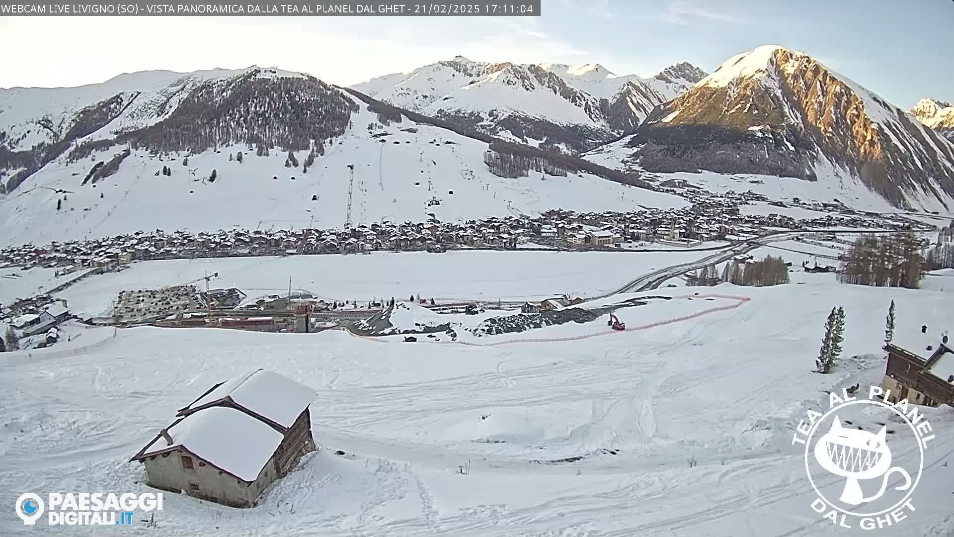 A snow-covered mountain village is nestled in a valley beneath snow-capped mountains on a sunny day.